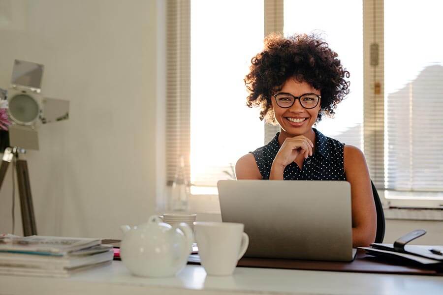 Portrait of smiling young woman sitting at her desk with laptop.